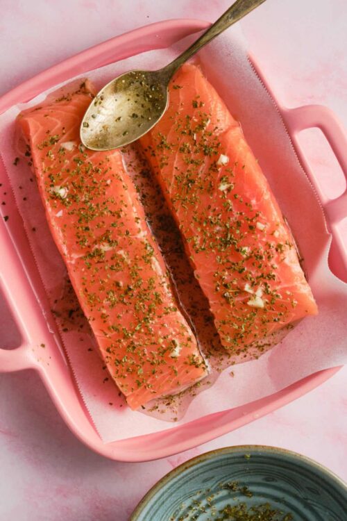 Juicy baked salmon fillets with herbs on pink baking dish.
