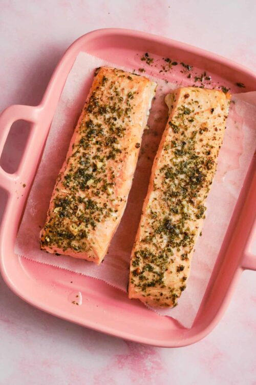 Tender baked salmon fillets with garlic and herb seasoning on a pink baking dish.