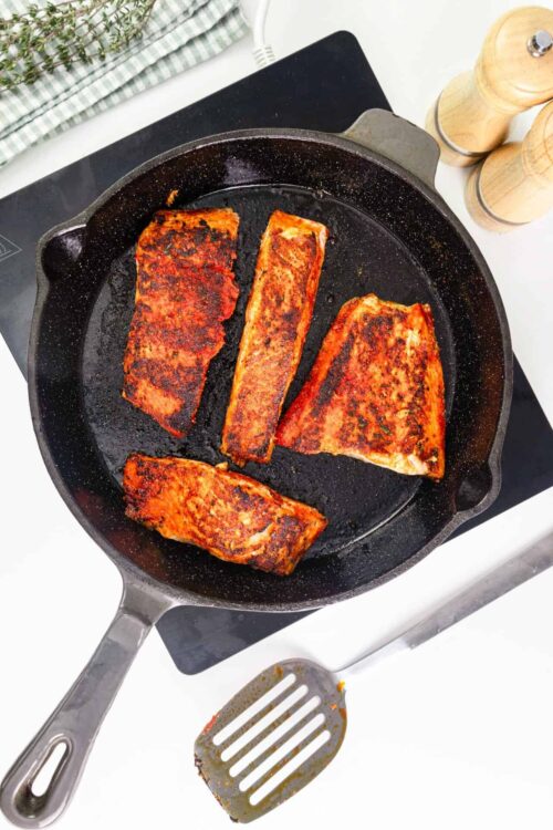 Seared salmon fillets cooking in a cast iron skillet with a flavorful crust.