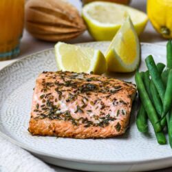 Juicy baked salmon with herbs served with lemon wedges and green beans on a textured plate.
