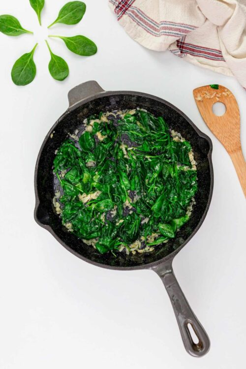 Fresh sautéed spinach with garlic in a black skillet, on white background.