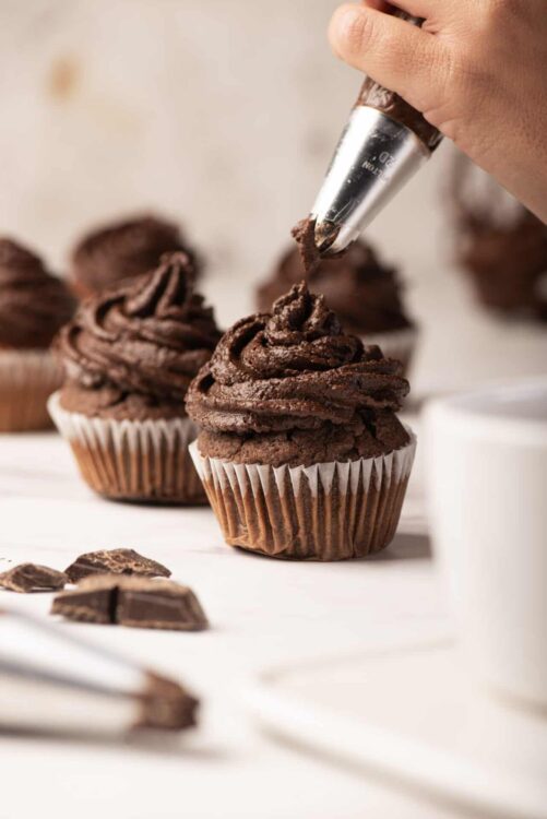 Cream-filled chocolate cupcakes with piping bag decorating them.