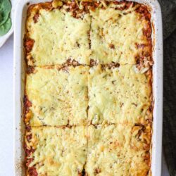 Baked cheesy beef enchiladas casserole in a white baking dish with melted cheese on top.