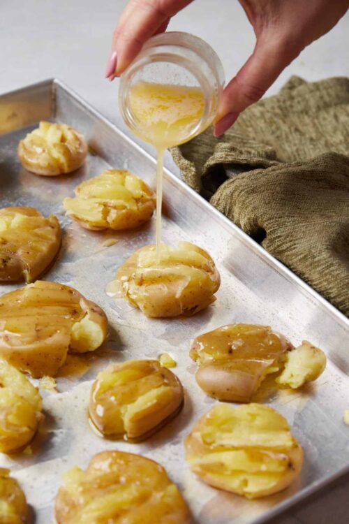 Buttered Hasselback Potatoes being drizzled with melted butter on a baking sheet.