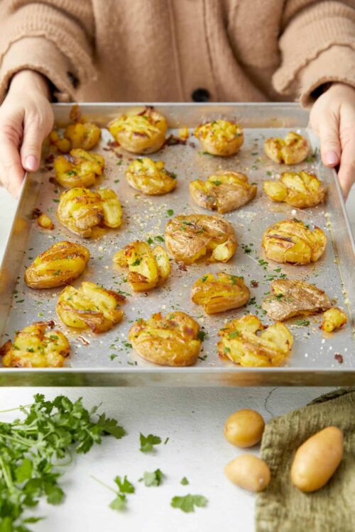 Golden roasted baby potatoes on baking sheet with herbs and garlic.