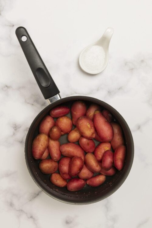 Fresh red mini potatoes in a black skillet on white marble surface.