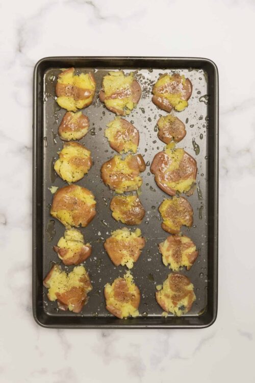Sweet potato halves baked on a black baking sheet with seasonings and oil.