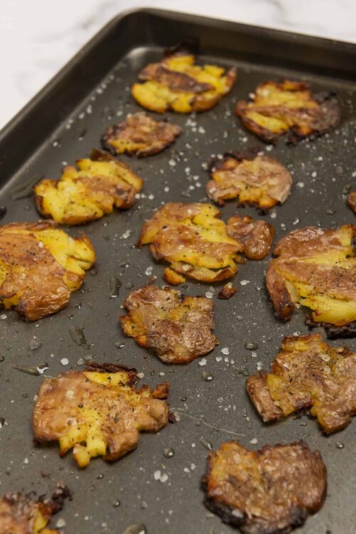 Crispy roasted potatoes with seasoned, golden-brown edges on a baking sheet. Perfect for comfort food recipes or side dishes.