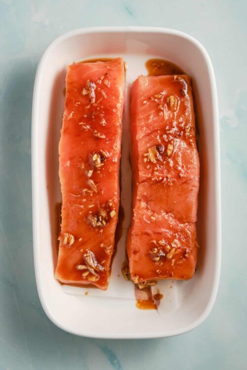 Sweet glazed salmon fillets topped with chopped nuts, served in a white dish.