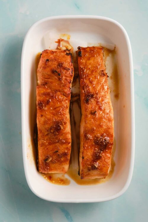 Baked salmon fillets with glazed, crispy top in a white baking dish.