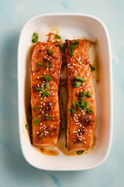 Salmon fillets with teriyaki glaze and sesame seeds on white dish.
