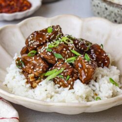 Savory beef tips over jasmine rice garnished with green onions and sesame seeds.