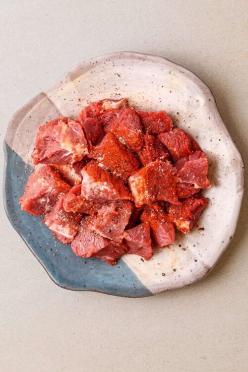 Fresh cubed beef seasoned for baking on a two-tone ceramic plate.
