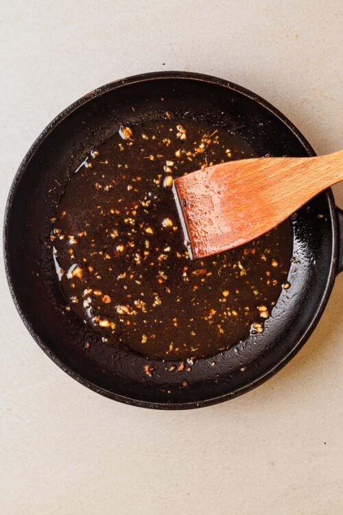 Honey garlic sauce cooking in a black skillet with a wooden spatula.