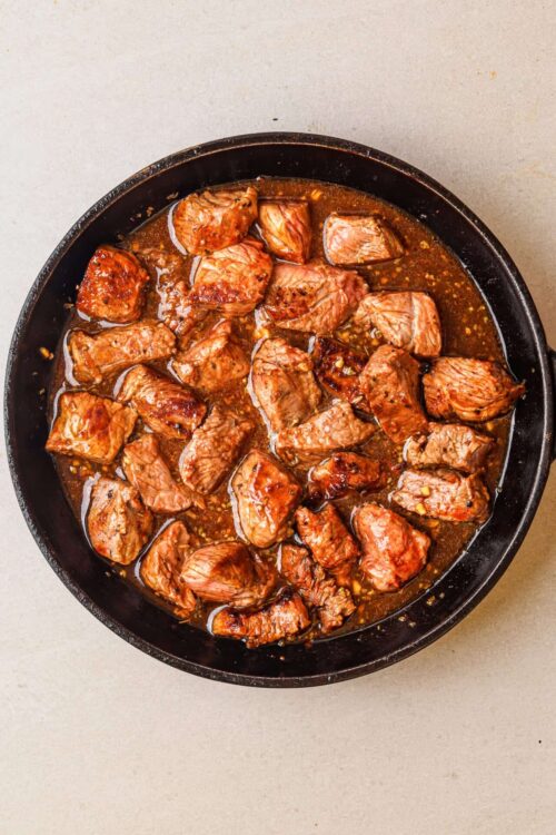 Juicy beef stew chunks cooking in rich, savory gravy in a black cast iron skillet.