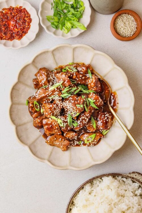 Stir-fried beef with Asian sauce, green onions, sesame seeds, served on a white plate.