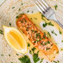Savory baked salmon fillet garnished with herbs and lemon wedge on a textured plate.