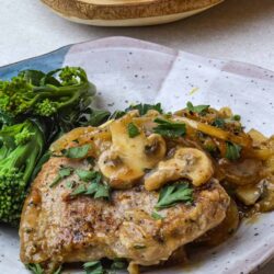 Succulent roasted chicken with mushroom gravy and fresh herbs, served with broccoli florets on a rustic bowl.