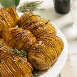 Crispy smashed potatoes with herbs and sea salt on a white platter.
