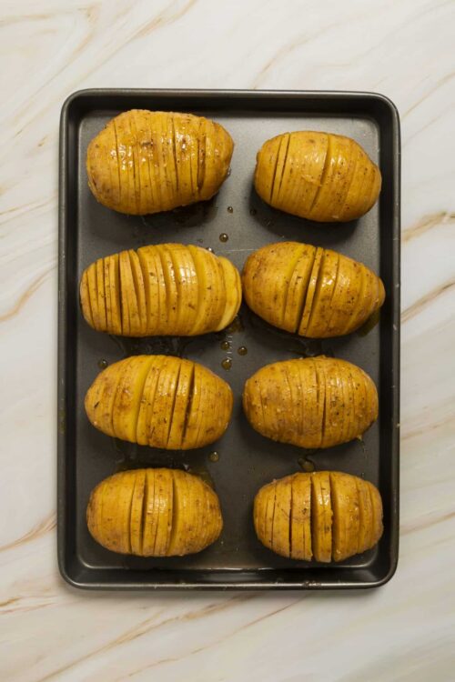 Baked Hasselback potatoes with crispy, seasoned skin on a baking sheet.