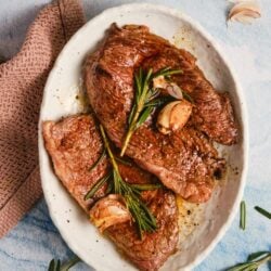 Juicy Cooked Ribeye Steak with Garlic and Fresh Rosemary on White Platter.