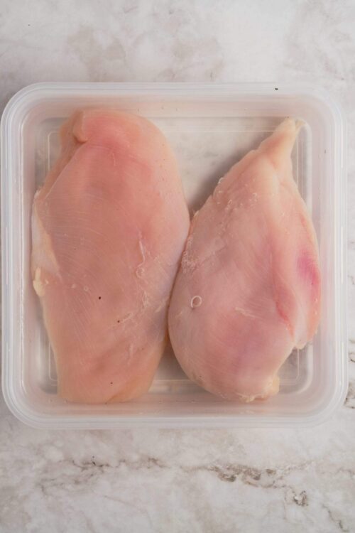 Raw chicken thighs in a plastic container ready for cooking or baking.