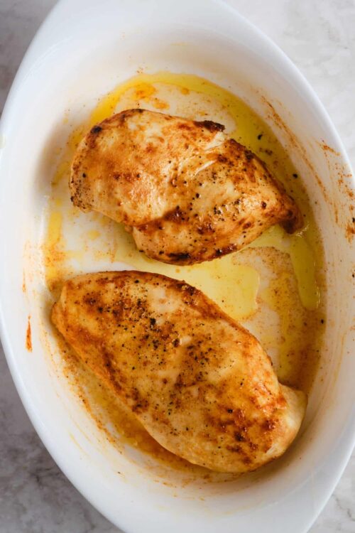 Juicy baked chicken breasts seasoned with spices in a white baking dish.