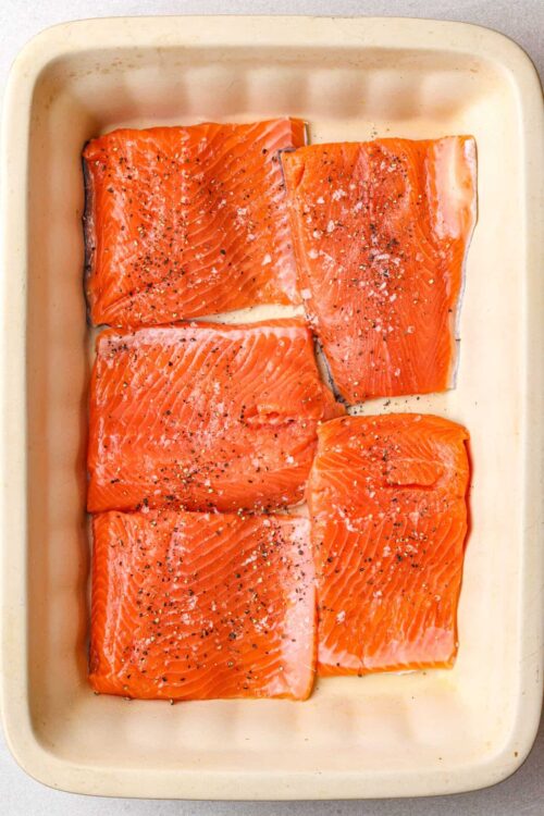 Fresh salmon fillets seasoned with salt and pepper in a baking dish, ready for cooking.