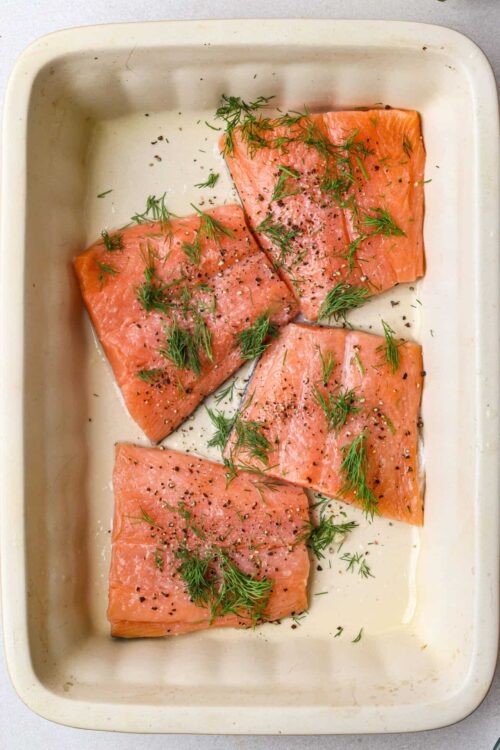 Salmon fillets with fresh dill and black pepper before baking.