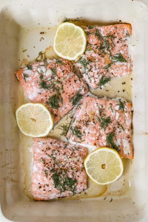 Fresh baked salmon fillets with lemon slices, dill, and pepper, ready for baking or serving.