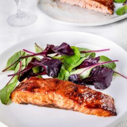 Grilled salmon with fresh mixed greens and a simple vinaigrette on white plate.