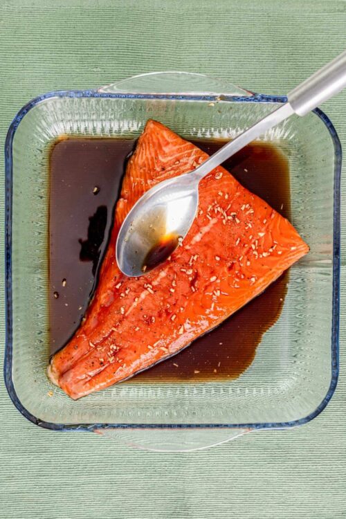 Salmon fillet marinating in soy sauce and garlic in a glass dish.