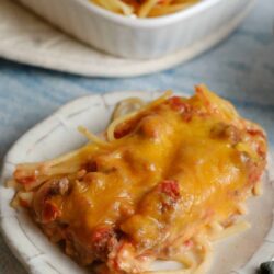 Cheesy baked spaghetti with meat sauce on a small white plate.