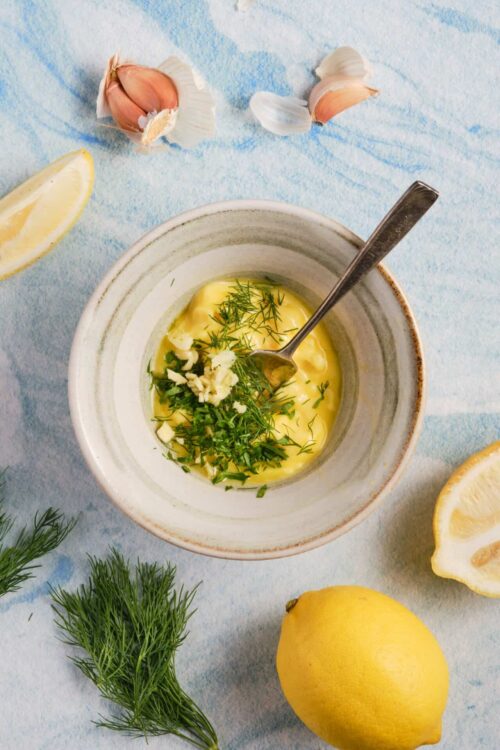 Lemon garlic herb sauce with fresh dill and garlic in a ceramic bowl on a textured blue background.