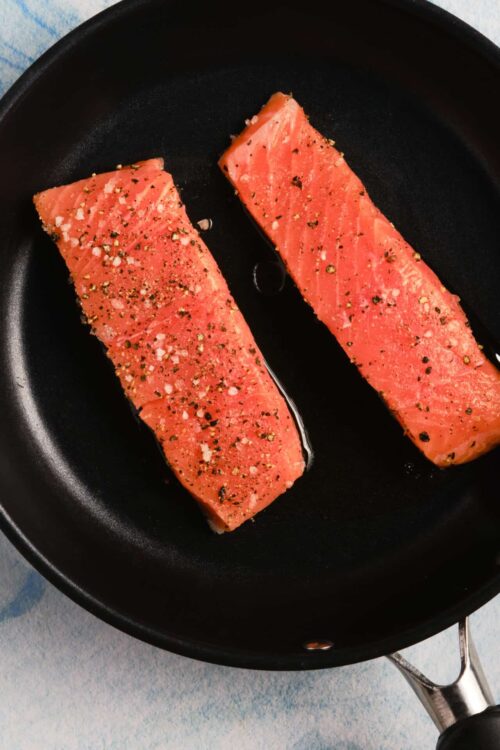 Juice salmon fillets seasoned with salt, pepper, and herbs in a non-stick skillet.