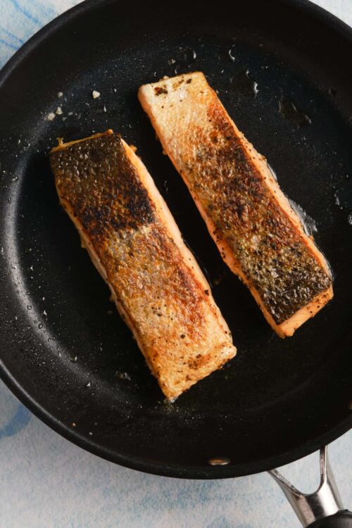 Golden brown seared salmon fillets in a black skillet.