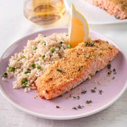 Baked salmon with crispy breadcrumb topping served with rice and lemon wedge on pink plate.
