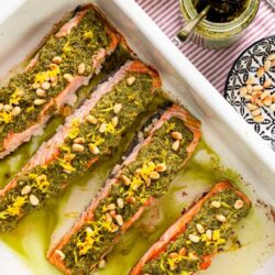 Baked salmon with chimichurri sauce garnished with lemon zest and pine nuts.