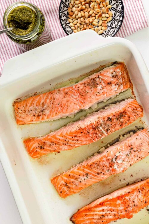 Baked salmon fillets with seasoning in a white casserole dish.