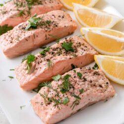 Juicy baked salmon fillets garnished with herbs and served with lemon wedges on a white plate.
