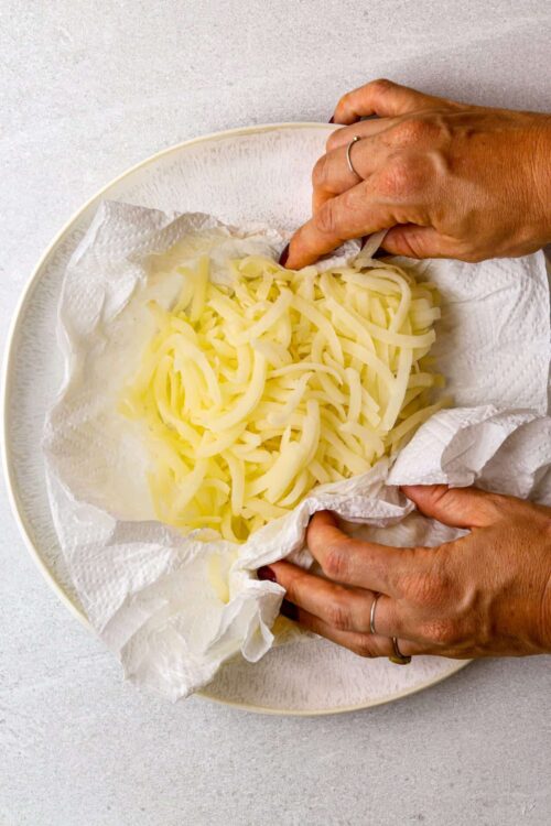 Shredded cheese being placed on paper towel-lined plate for baking or cooking prep.