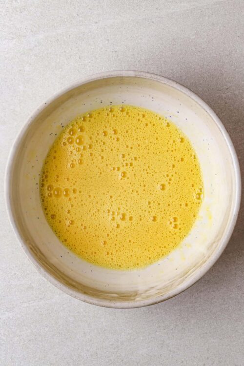 Smooth beaten eggs in a white bowl for baking or cooking.