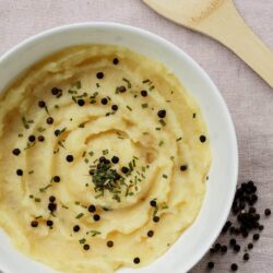 Creamy mashed potatoes with black pepper and chopped chives in a white bowl.