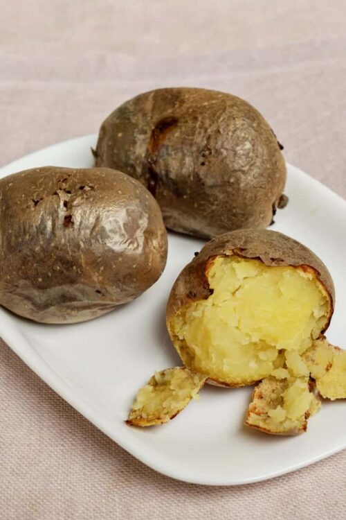 Baked russet potatoes with fluffy interior on white plate.