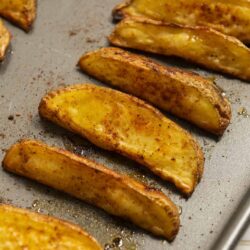 Golden roasted potato wedges on baking sheet, crispy and seasoned.