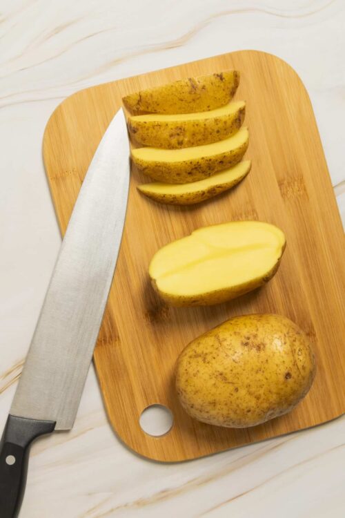 Fresh yellow potatoes sliced on cutting board for homemade baked potato recipe.