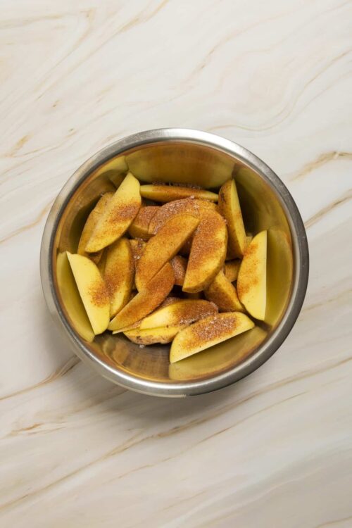 Sliced apples in a stainless steel bowl with cinnamon and sugar for baking or cooking.