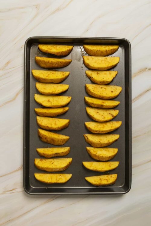 Baked potato wedges seasoned with spices on a baking sheet.
