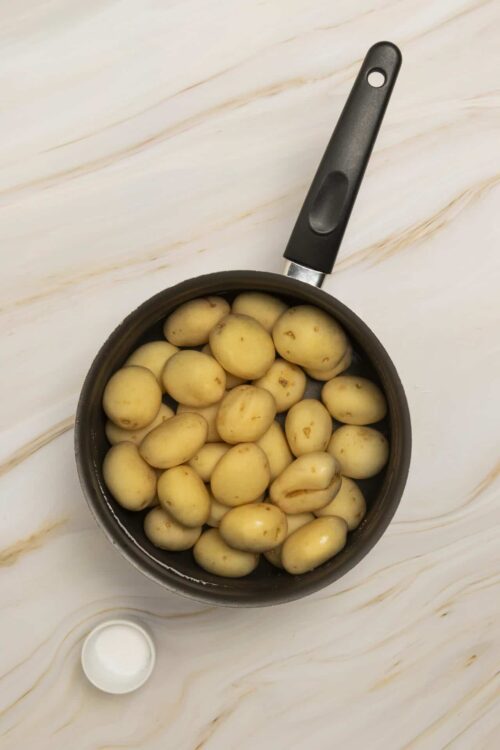 Golden roasted baby potatoes in a black skillet with a small bowl of milk on a marble countertop.