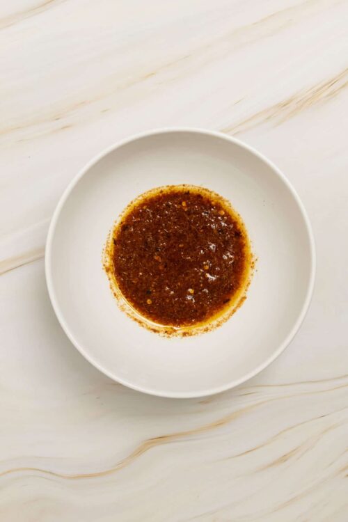 Spicy chili oil in a white bowl on marble countertop.